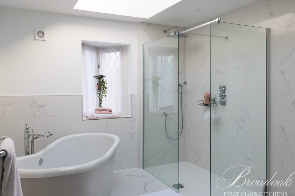 Modern white bathroom with freestanding bathtub and spacious glass-enclosed shower, featuring elegant marble tiles and natural light from a window with sheer curtains, showcasing luxury bathroom design.