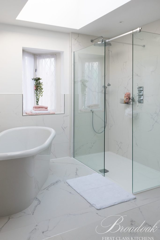Sleek white bathroom featuring a modern walk-in shower with glass enclosure, freestanding bathtub, and marble-effect tiles, showcasing luxury bathroom design by Broadoak Kitchens Ltd.