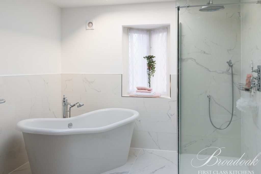 Luxurious white freestanding bathtub in a modern bathroom with marble tiles, natural light from window, and elegant design, showcasing high-quality bathroom fixtures and contemporary style.
