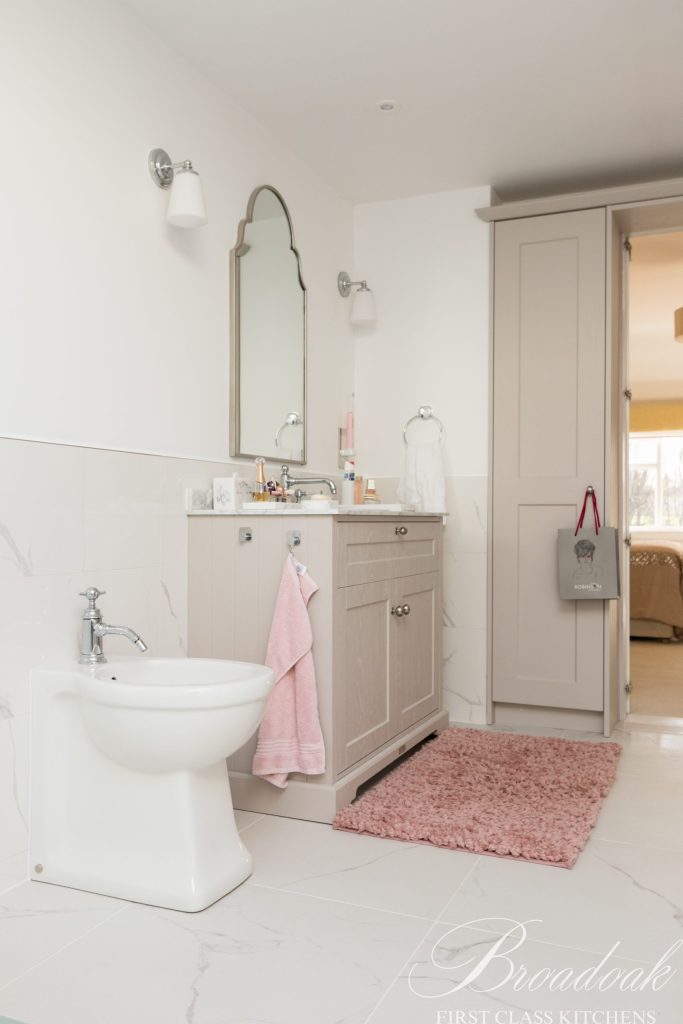 Modern beige bathroom vanity with marble countertop, white bidet, pink towels, and wall-mounted mirror, part of Broadoak Kitchens' bespoke bathroom design services.