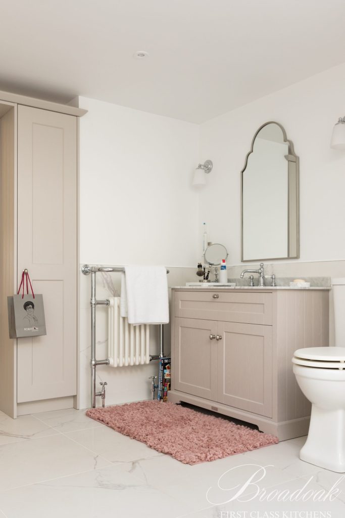 Elegant bathroom vanity with beige shaker-style cabinet, marble countertop, and classic mirror; part of Broadoak Kitchens Ltd's bespoke home design solutions.