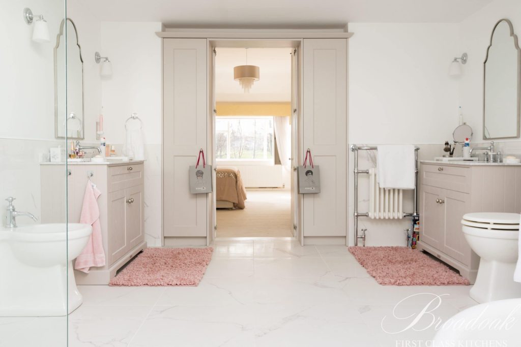 Bright and spacious white bathroom featuring classic cabinetry, dual sinks, modern fixtures, and soft pink rugs, showcasing high-quality kitchen and bathroom designs by Broadoak Kitchens Ltd.