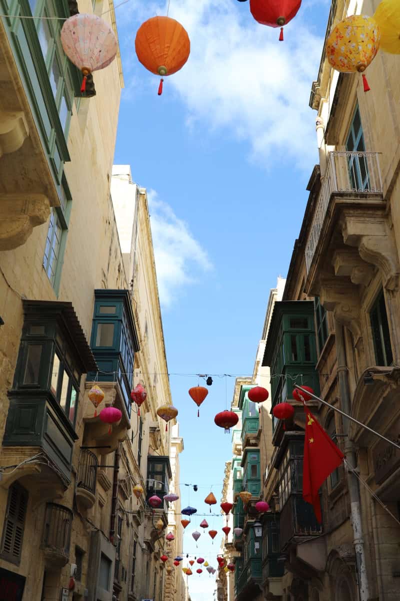Colourful lanterns hanging over narrow street in Valletta Malta, showcasing vibrant cityscape and historic architecture.