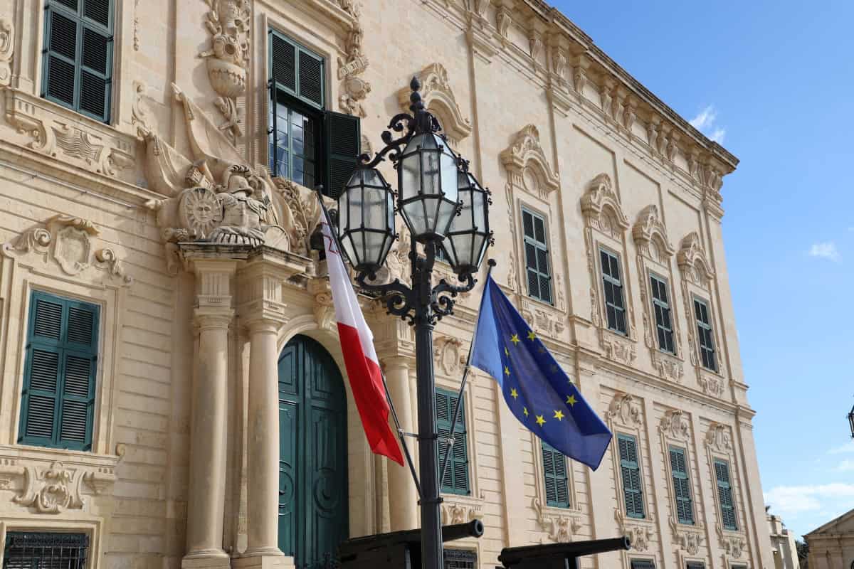 Beautiful historic building in Malta with flags and ornate architecture, part of The Wandering Woodward travel blog.