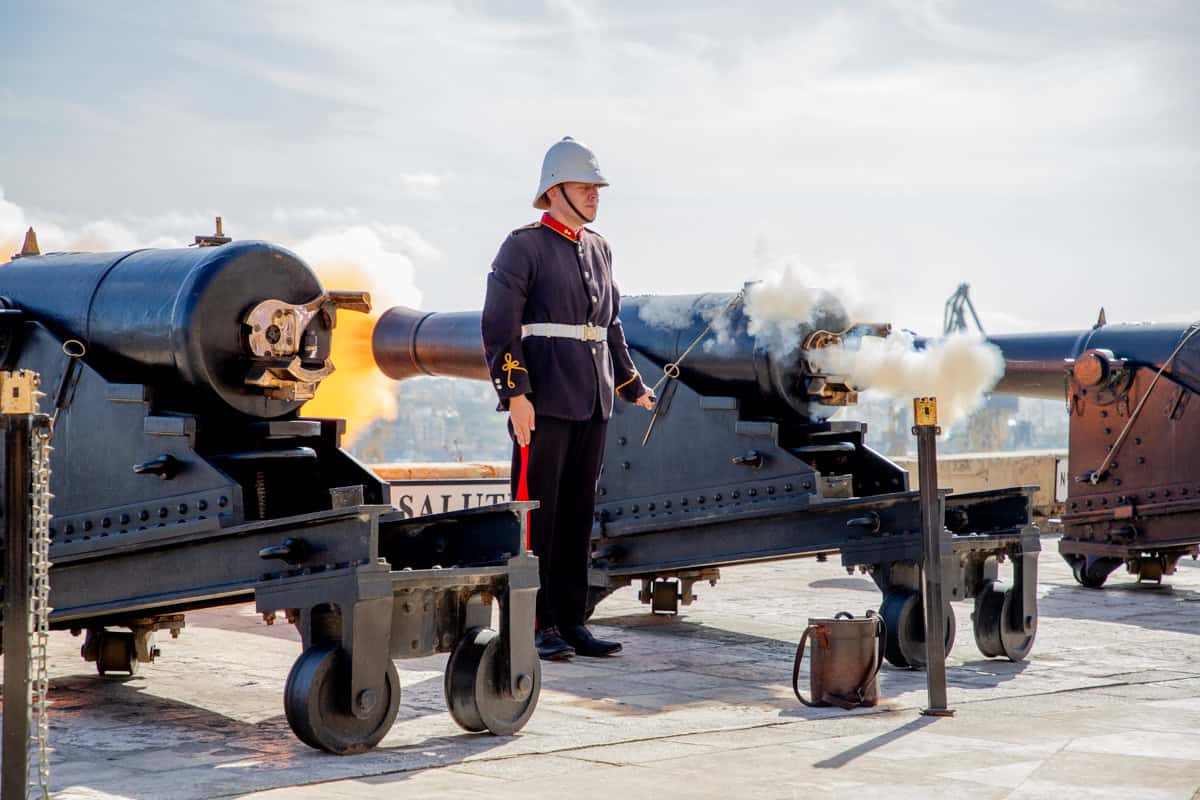 Historical cannon firing demonstration with a uniformed soldier on a historic fortress.