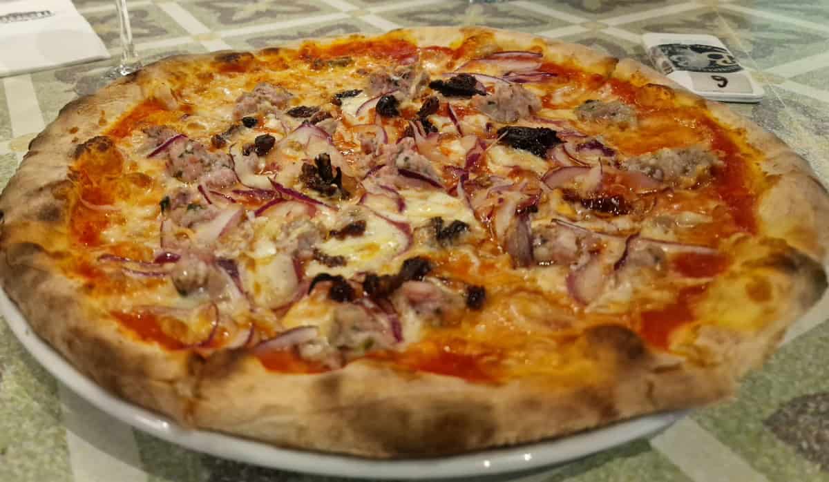 Fresh homemade meat pizza with melted cheese and toppings on a ceramic plate.