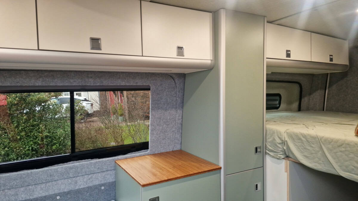 Compact camper van interior with storage cabinets and sleeping area, ideal for adventure travellers.
