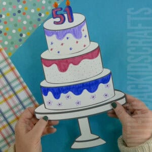 A colorful paper craft of a three-tiered birthday cake craft, decorated with markers and placed on a stand, made using a free printable for kids.