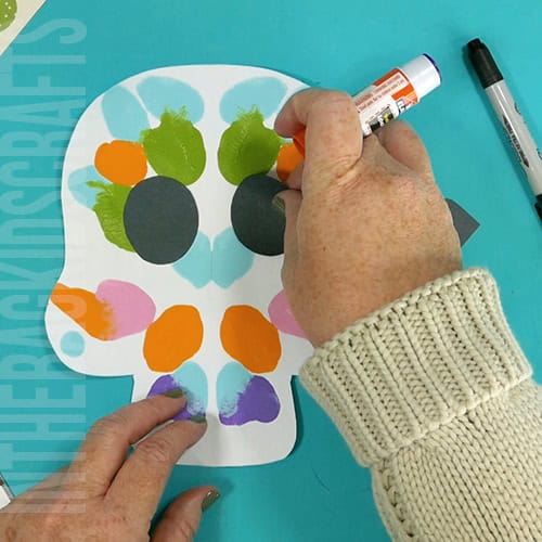 An image showing a colorful paper skull craft for kids, perfect as a Day of the Dead craft activity. step 5 glueing the pieces in place 