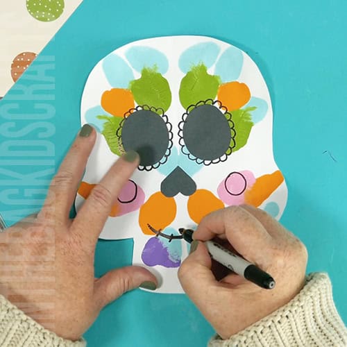 An image showing a colorful paper skull craft for kids, perfect as a Day of the Dead craft activity.  step 6 drawing in details 