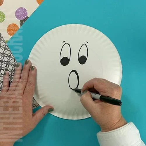 An image showing a simple paper plate ghost craft, perfect for an easy Halloween craft and fun preschool activity for kids. step 1 drawing the face