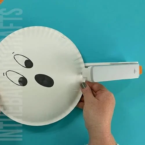 An image showing a simple paper plate ghost craft, perfect for an easy Halloween craft and fun preschool activity for kids. step 3 stapling the plates together 