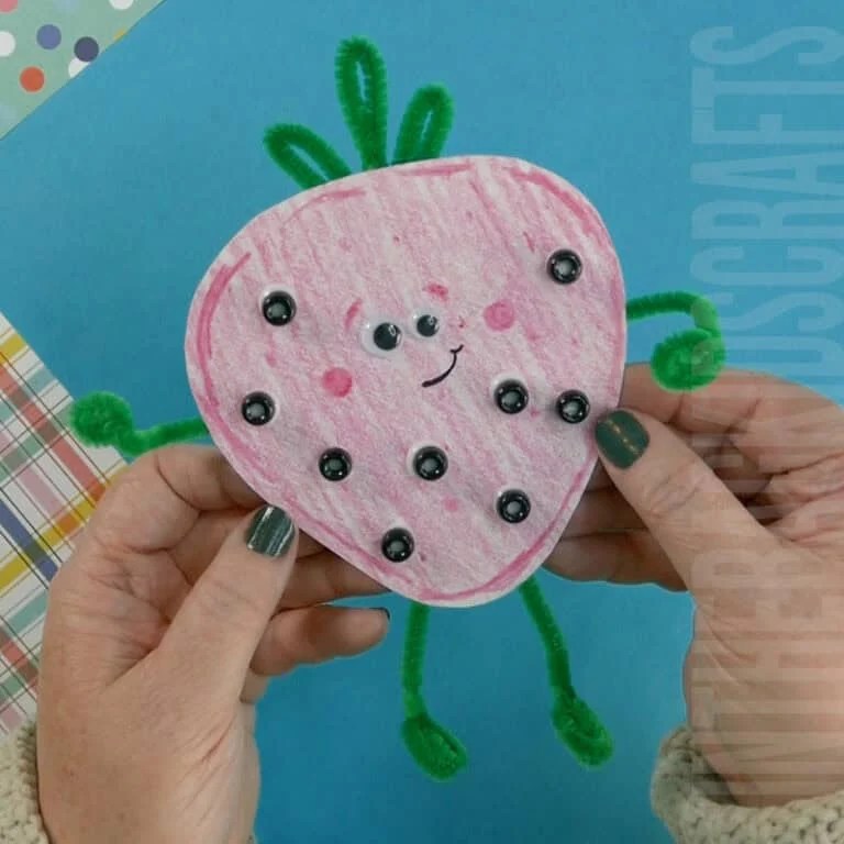 A fun and easy strawberry craft made with pink coloring, green pipe cleaners, and black beads, perfect as a spring craft for kids.