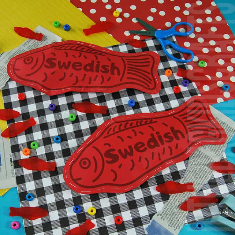 A colorful candy craft featuring a Swedish Fish paper craft for kids, with red fish-shaped cutouts, real gummy candies, craft supplies, and decorative backgrounds.