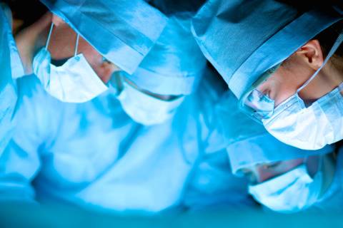 Surgical team in scrubs and masks performing a medical procedure in the operating room.