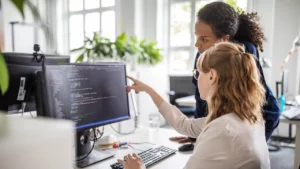 Two women collaborating on software testing and validation at a computer workstation.