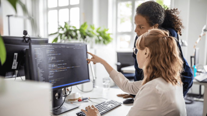 Two women collaborating on software testing and validation at a computer workstation.