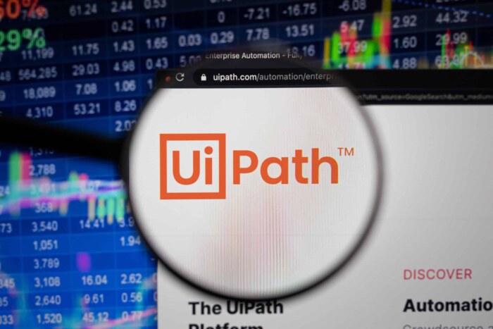 UiPath logo magnified over stock market data and Excel spreadsheets for automation.