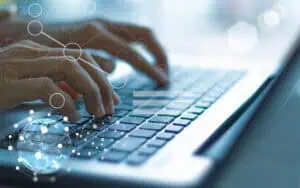 Hands typing on a laptop keyboard with digital network graphics overlay.