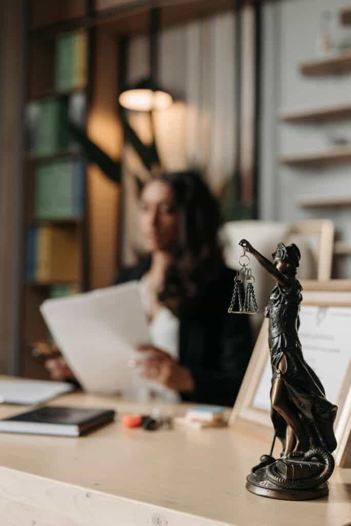 Woman sitting at desk with bronze figure of justice and balanced scales in foreground