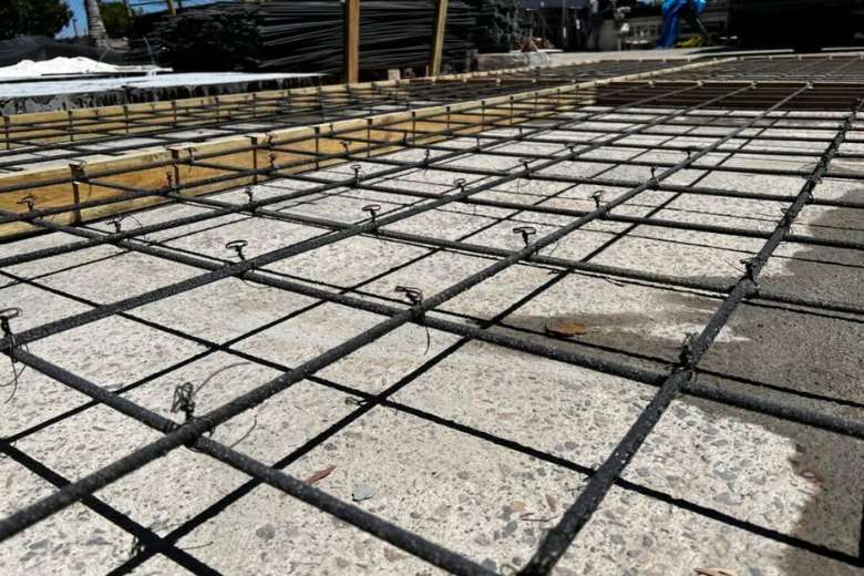 Construction site photo showing fiberglass rebar grid secured with white plastic rebar chairs spaced 600mm apart and tied with plastic zip ties to prevent floating during concrete pour