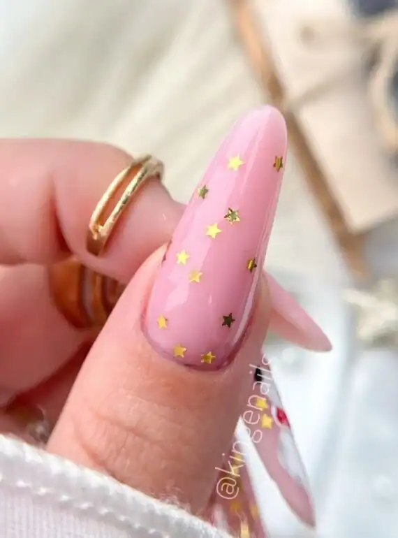 Roze nagel met gouden sterren en glans, perfect voor feestelijke gelegenheden.