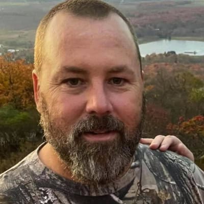 A man with a beard standing next to a lake.
