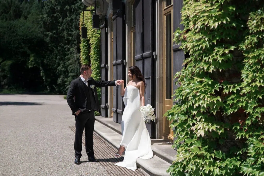 Hochzeitspaar bei emotionalem Moment vor einem modernen Gebäude, Natur im Hintergrund.