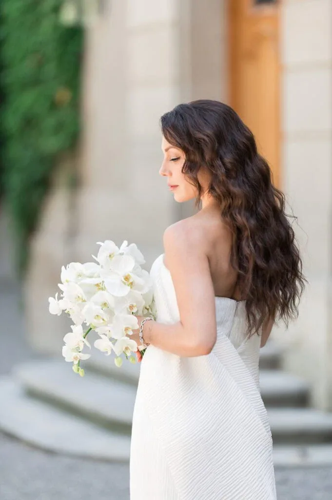Frau in weißem Brautkleid hält Blumenstrauß bei Hochzeit im Freien.