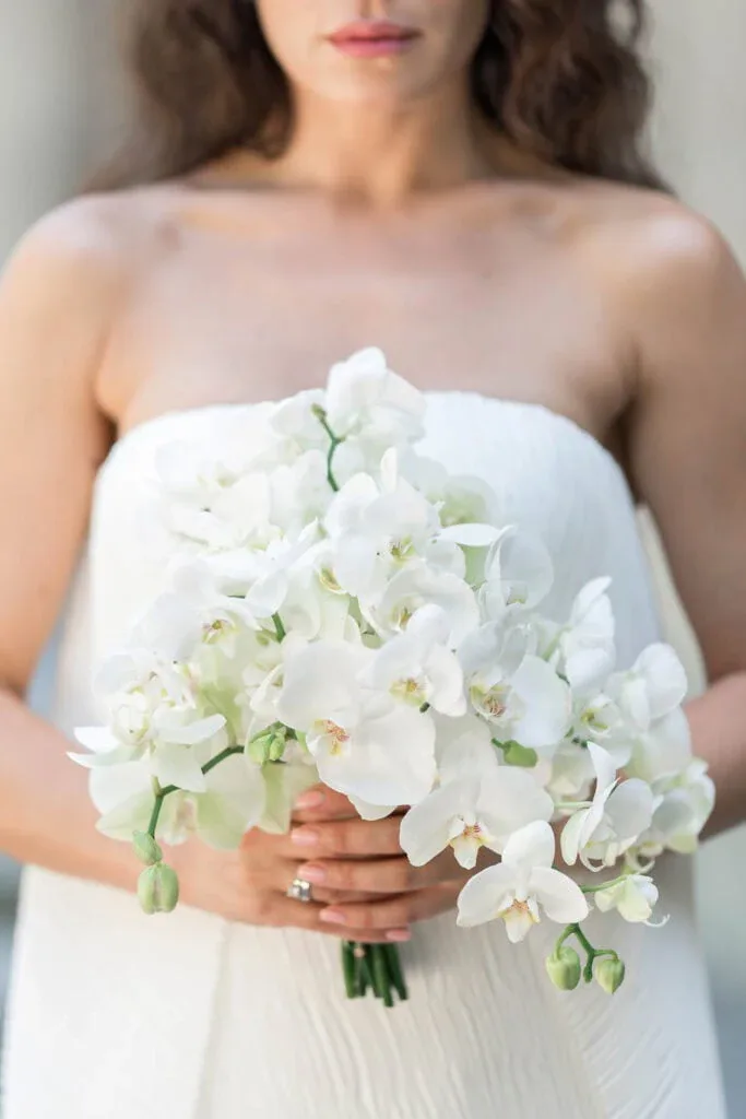 Braut hält weißen Orchideenstrauß bei Hochzeitsfotografie.