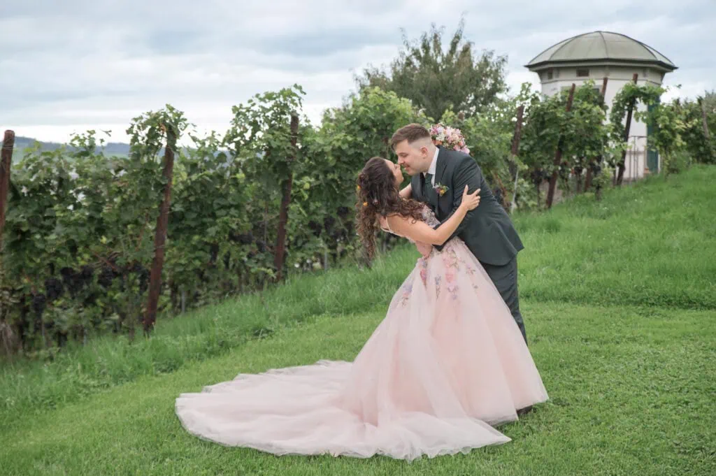 Hochzeit im Freien: Braut und Bräutigam tanzen auf einer Wiese mit Weinreben im Hintergrund.