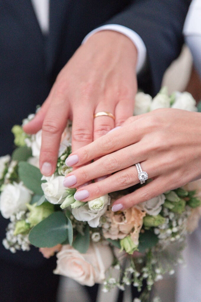 Nahaufnahme der Hände mit Ehering und Blumenstrauß bei einer Hochzeit.