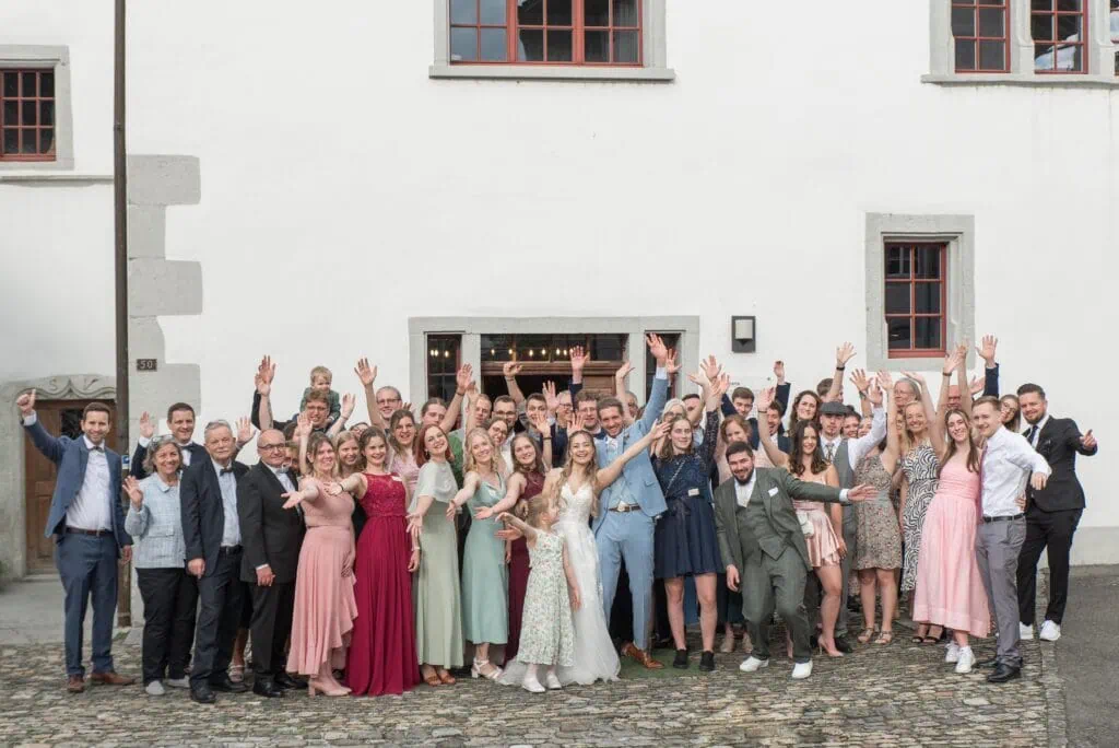 Fröhliche Hochzeitsgesellschaft vor einem weißen Gebäude mit cobblestone Boden.