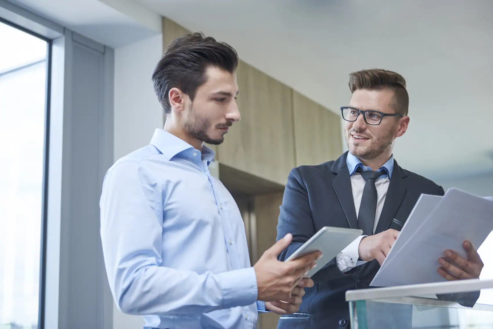 Dos hombres de negocios colaborando mientras revisan documentos y una tableta, representando el concepto de qué es el ENS y su cumplimiento en entornos corporativos.