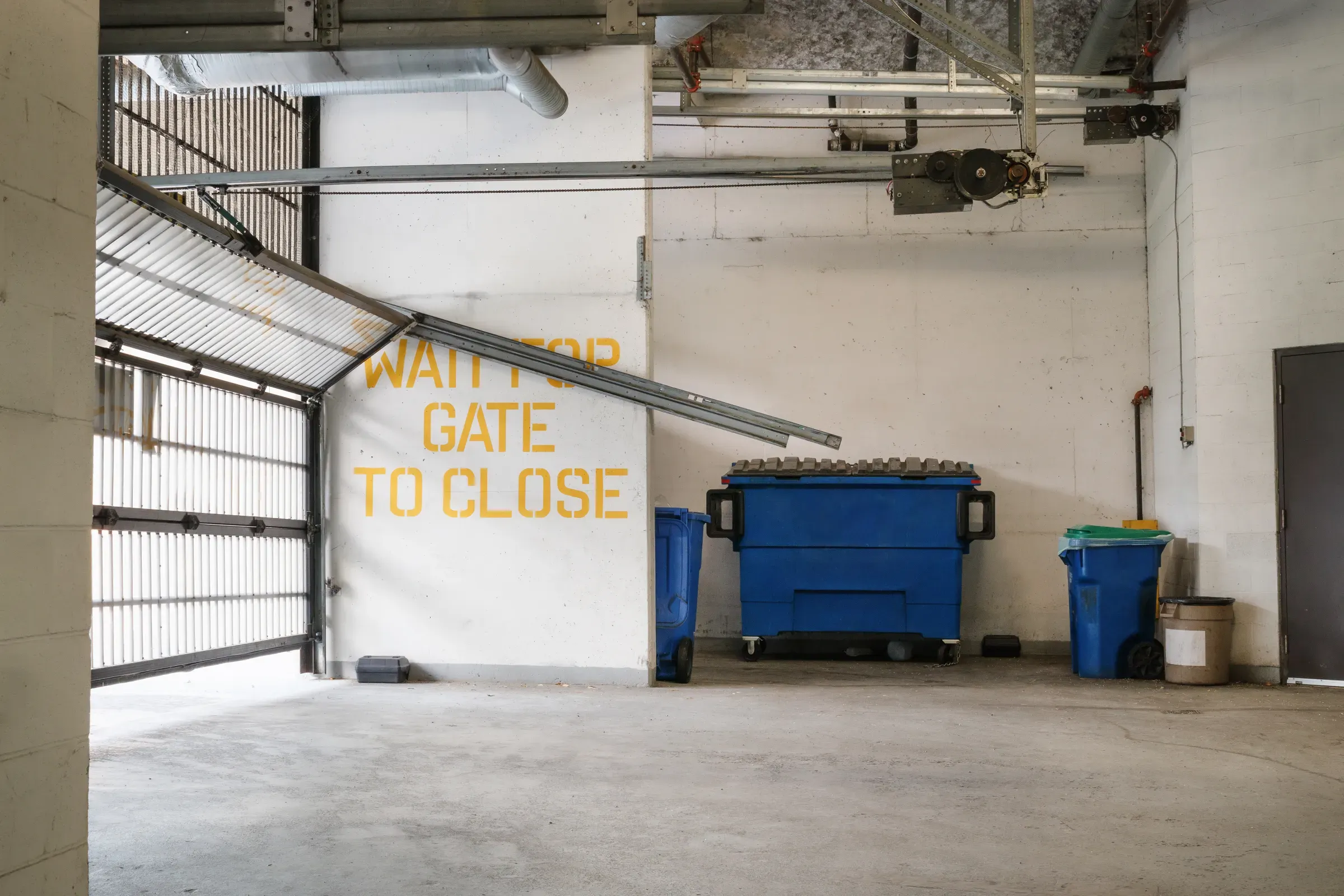 Parking garage with gate and waste bins in residential strata complex.