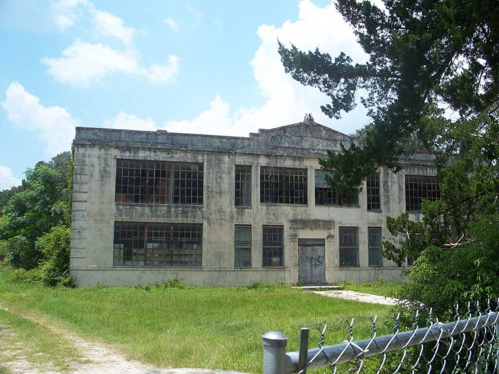 Decaying abandoned industrial building with broken windows and overgrown surroundings.