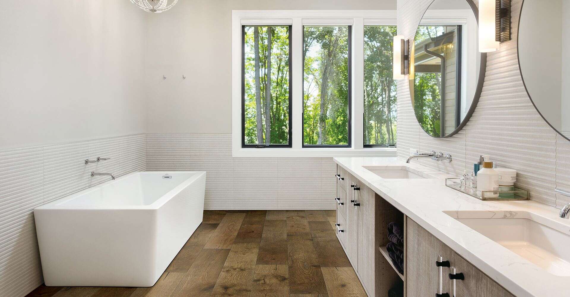 Bright bathroom featuring a sleek bathtub, double vanity, and large window overlooking greenery, creating a relaxing and airy atmosphere.