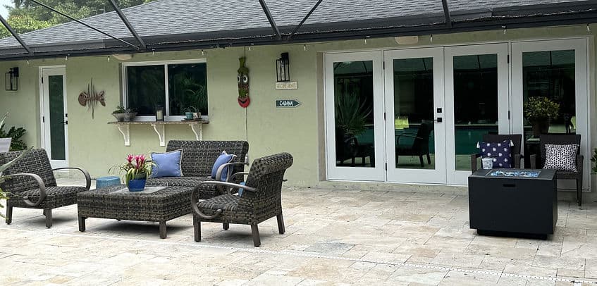 Outdoor patio with wicker furniture, cushions, and potted plants in a residential backyard.