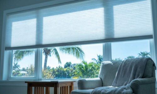 Bright living room with large window overlooking tropical palm trees and lush greenery, featuring a comfortable armchair and a small wooden side table.