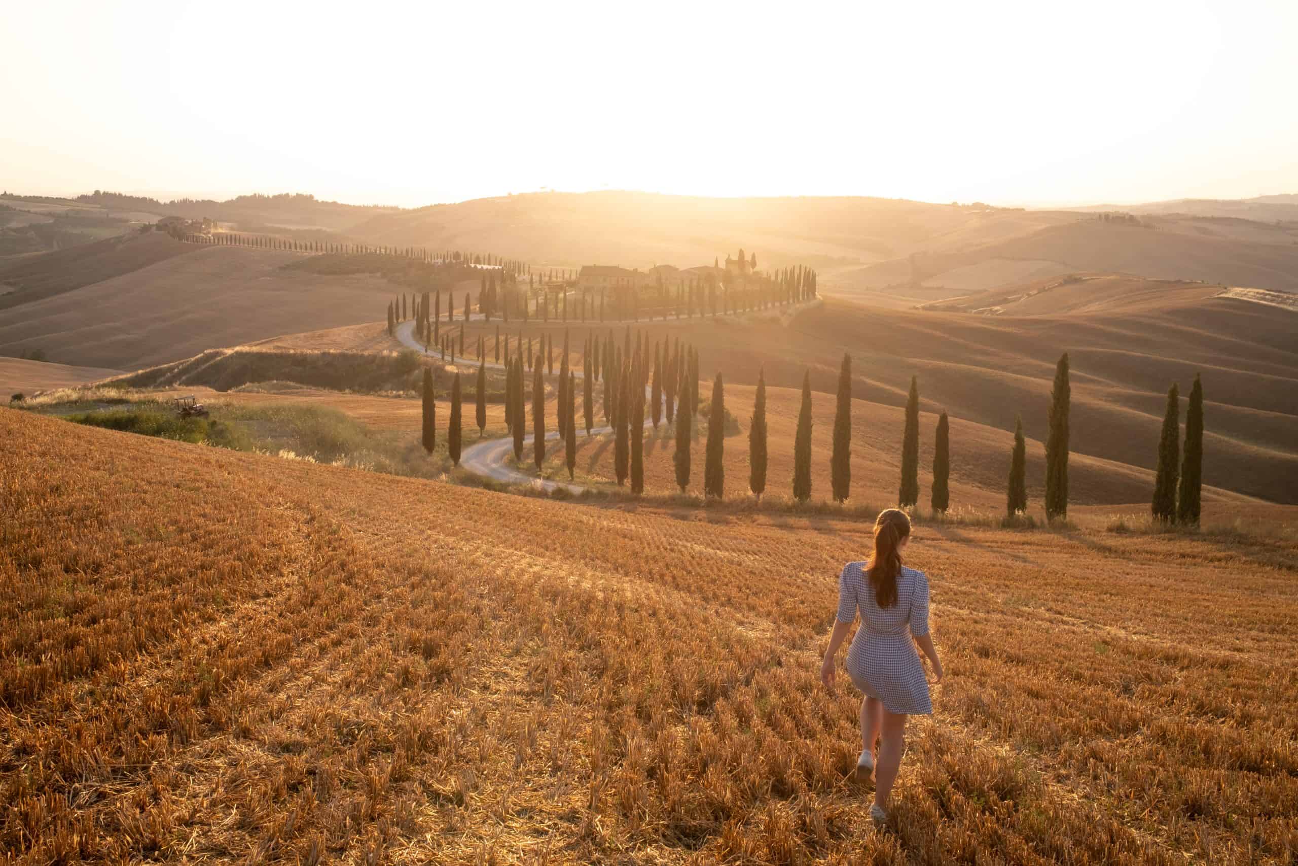 Gaia walking in the hills in Tuscany at sunset in front of a row of cypresses