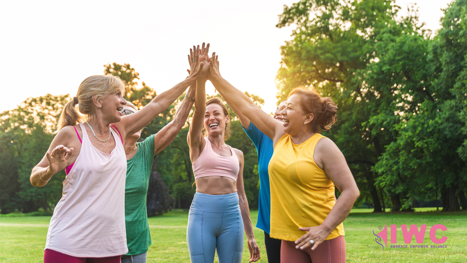 Diverse group of women smiling and high-fiving outdoors in the sunshine, representing joyful movement and wellness at Island Wellness Clinic.