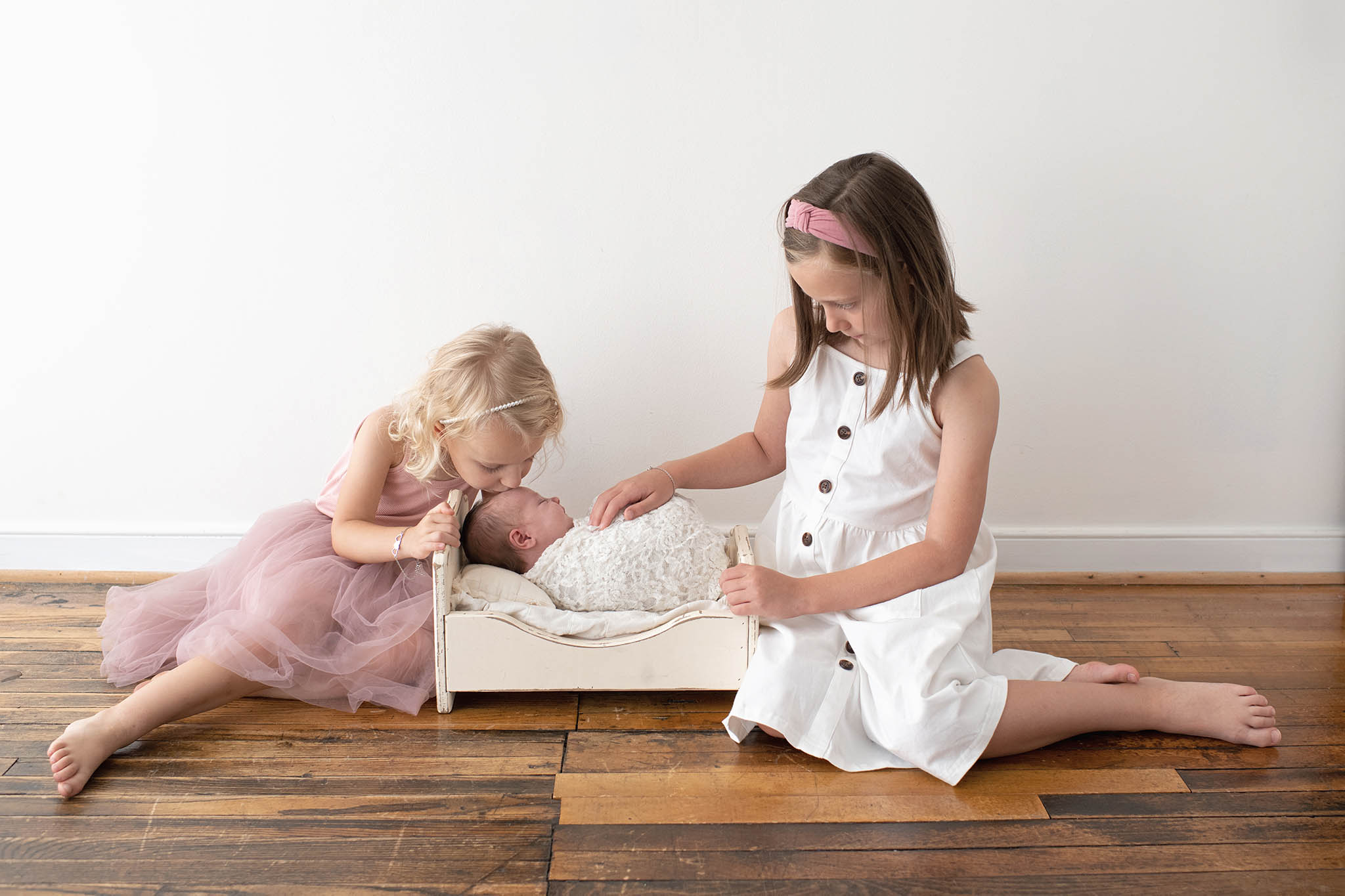 Two young sisters gazing at and kissing their newborn sibling