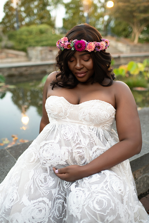 Expecting mother in a white flowing maternity gown walking along Carroll Creek in Frederick Maryland during outdoor maternity photos