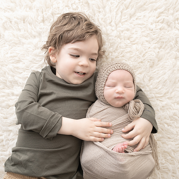 Siblings in neutral colors snuggling newborn baby during photography session