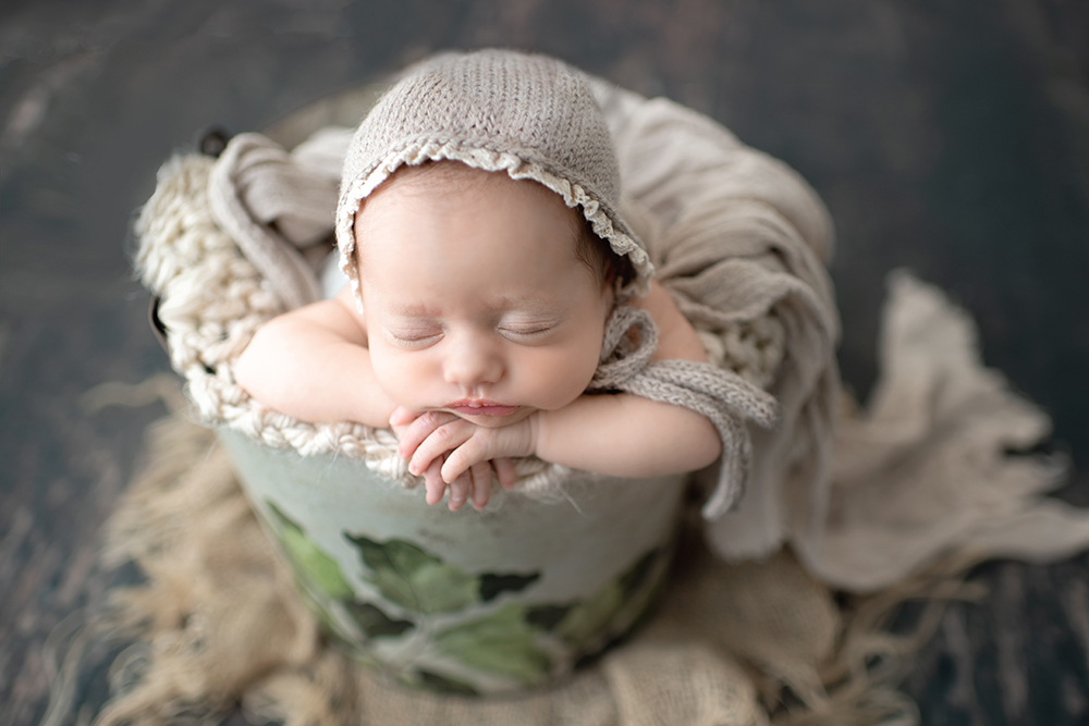 newborn baby girl in bucket with knitted tan hat