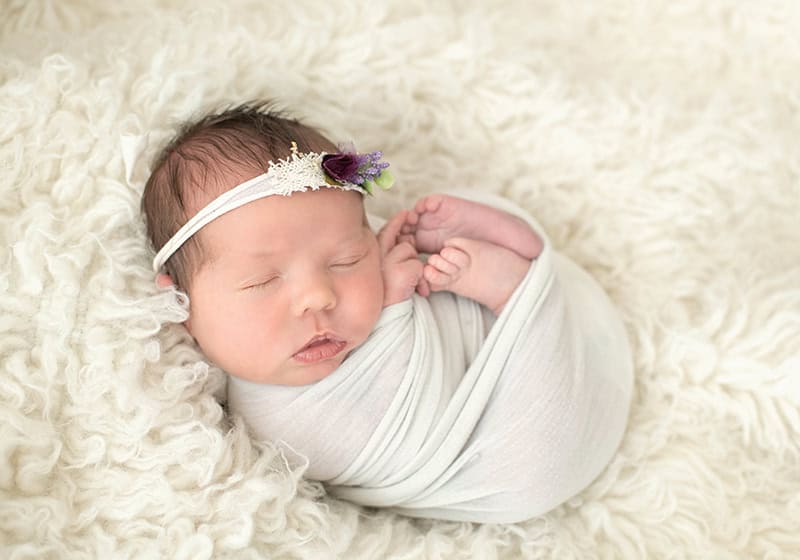 neutral swaddled baby girl on cream flokati