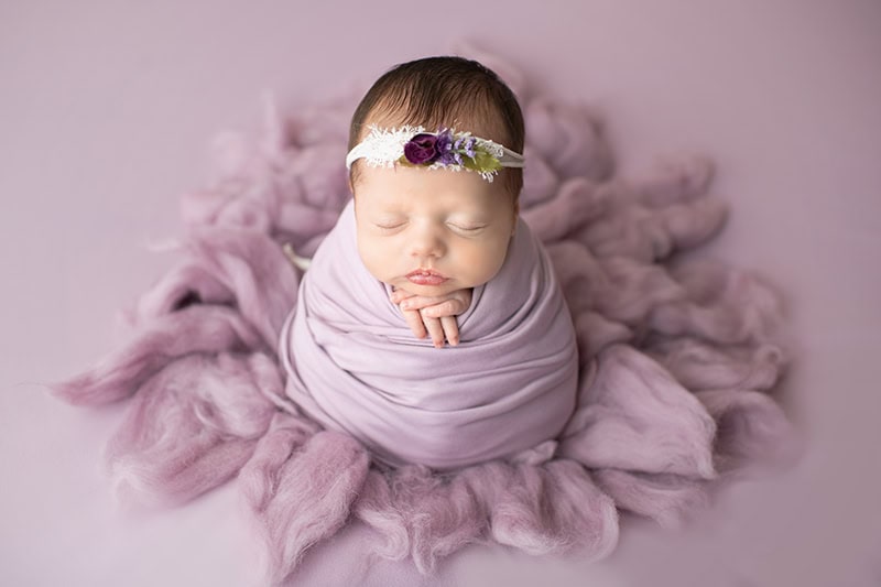 baby girl with lavender swaddle and matching headband in frederick md newborn photography studio