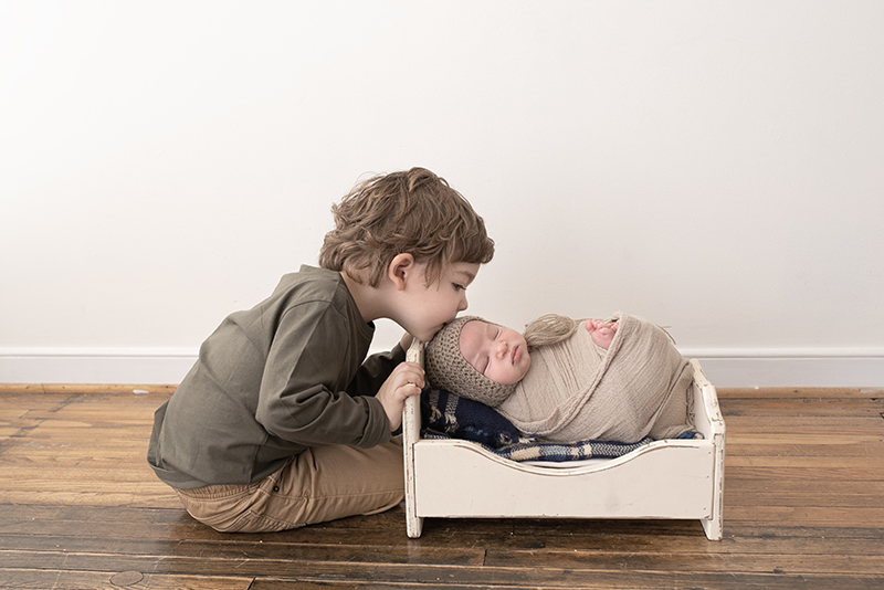 newborn in tiny bed being kissed by his big brother
