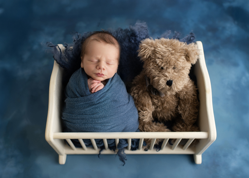 baby in cradle with teddy bear in all blue
