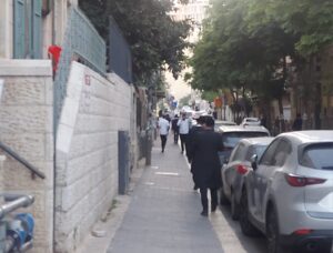 גברים חרדים הולכים בשקט ברחוב מוצל בירושלים, לקראת ערב